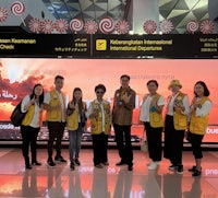 a group of people posing in front of an airport sign